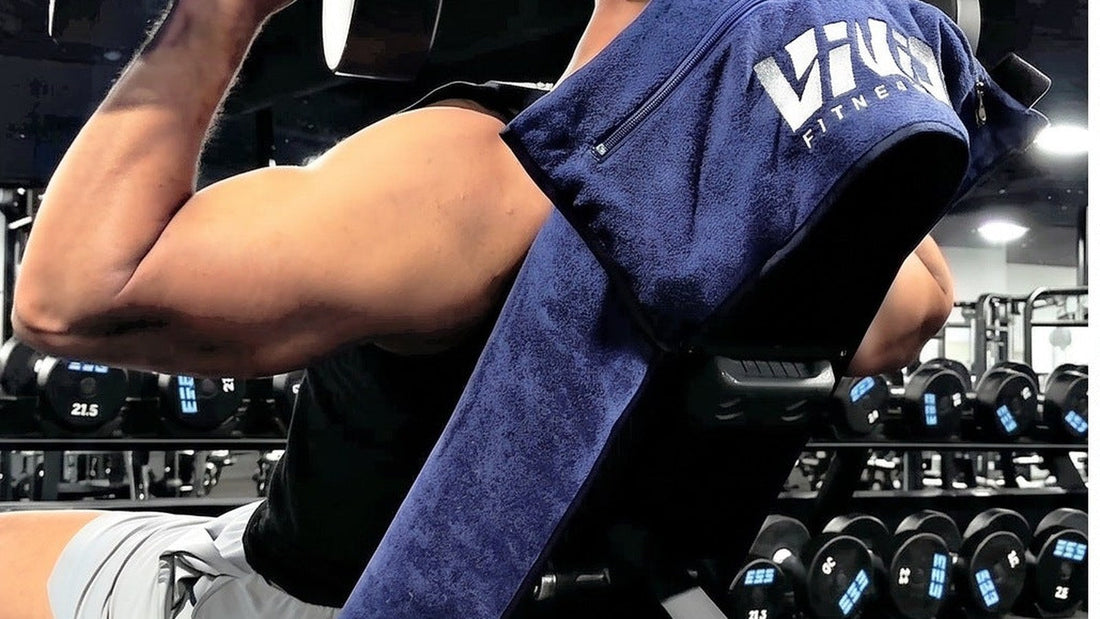 Navy VIVID hooded gym towel hooked over an incline bench during a dumbbell press