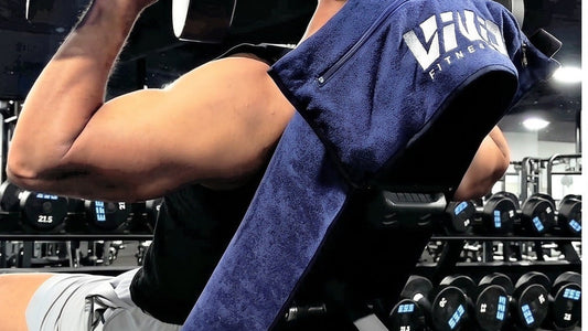 Navy VIVID hooded gym towel hooked over an incline bench during a dumbbell press