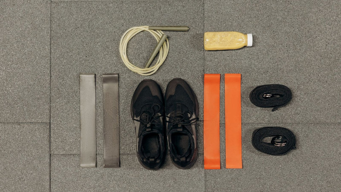 Gym shoes, resistance bands, a skipping rope and a drink laid out on a gym floor