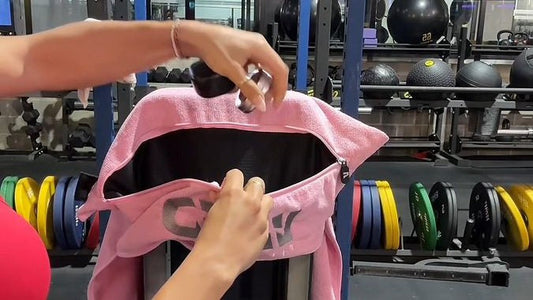 Hands hooking the hood of a pink VIVID hooded gym towel over the top of a gym bench