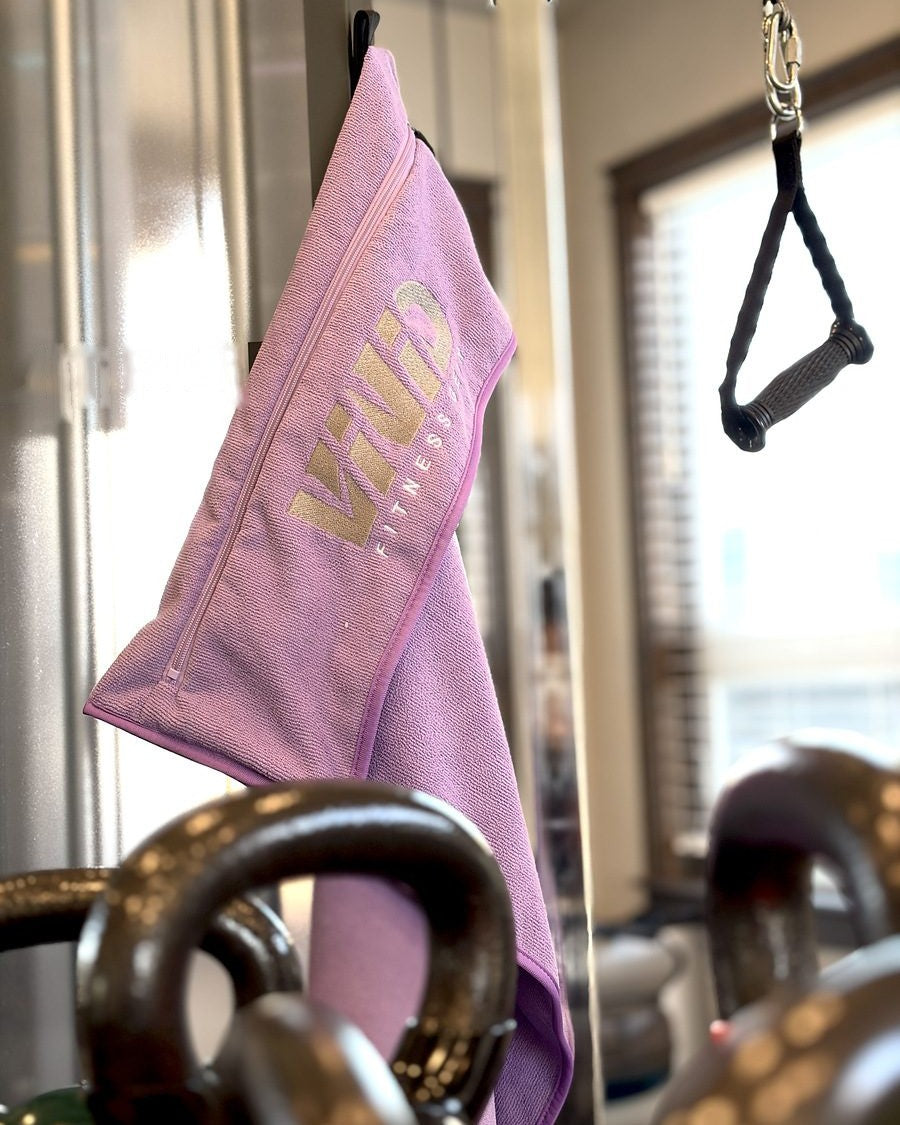 Purple VIVID gym towel hanging by its magnet strap on a steel cable machine